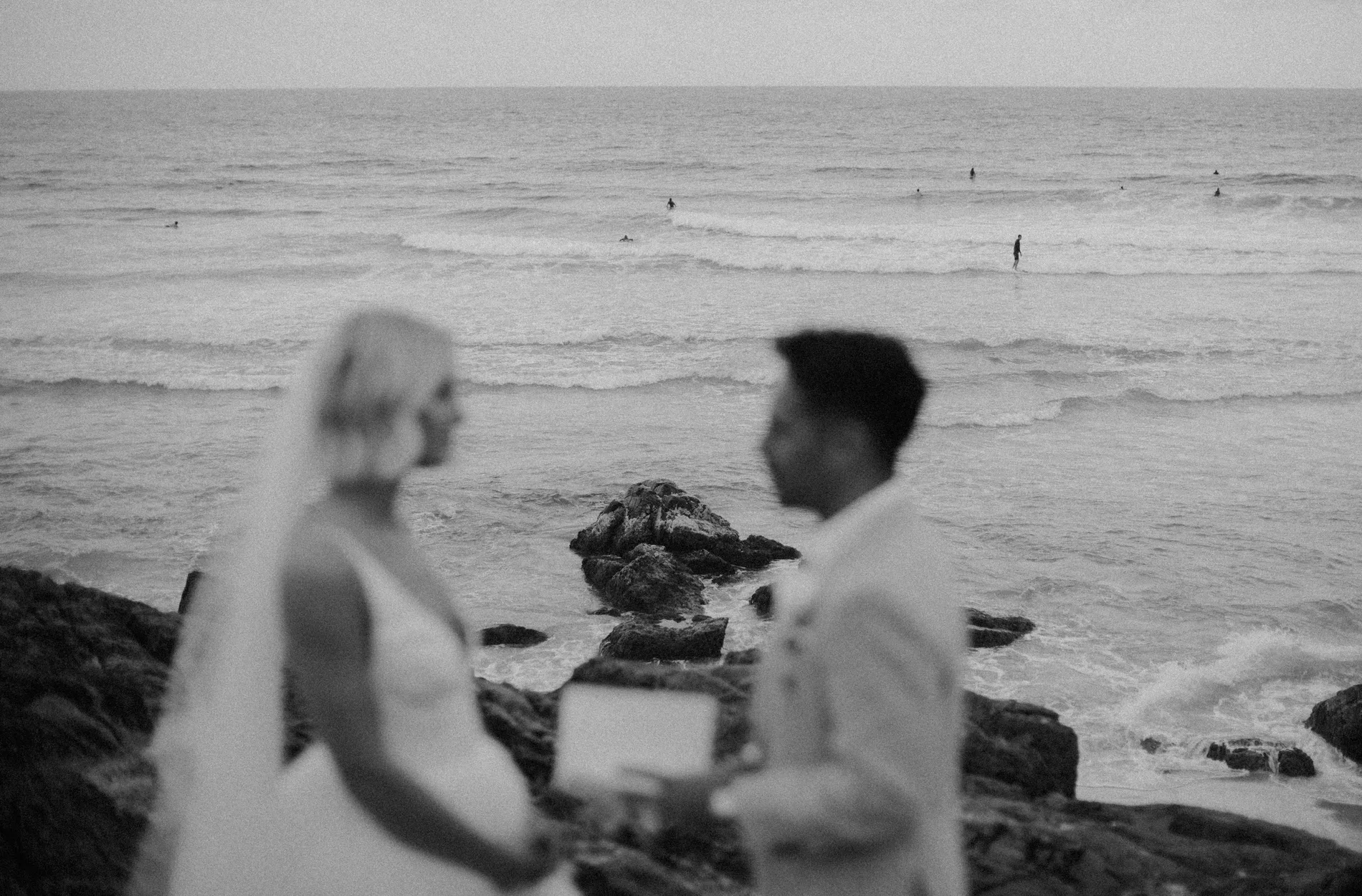 Black and white frame of a couple with the surf behind them