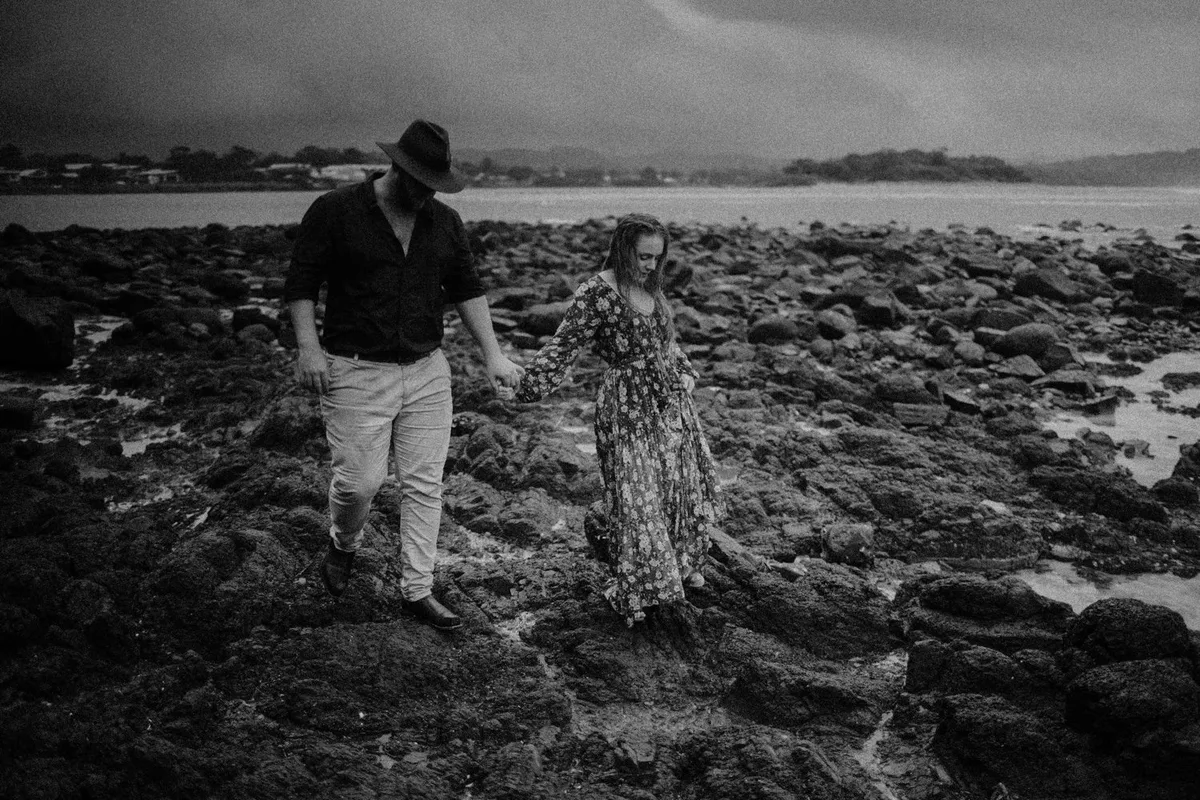 A couple walking across wet rocks at the ocean's edge