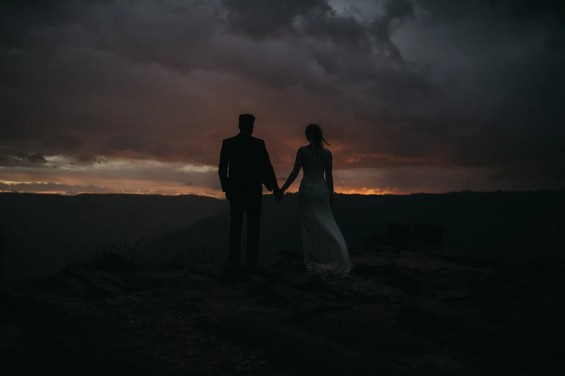 A couple silhouetted against a storm-lit ridge at dusk
