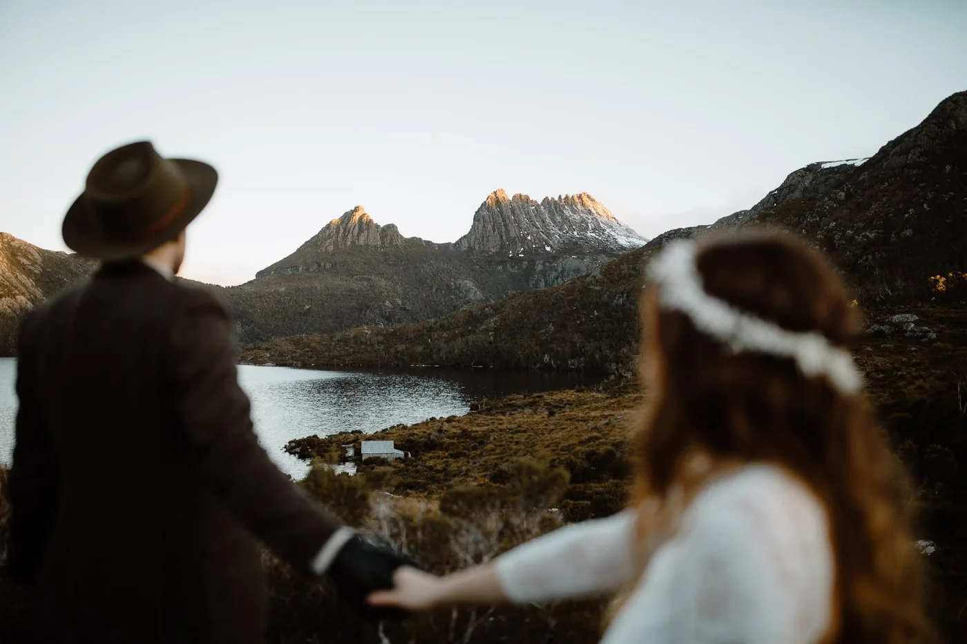 Josh and Tess reaching for each other in front of a mountain range