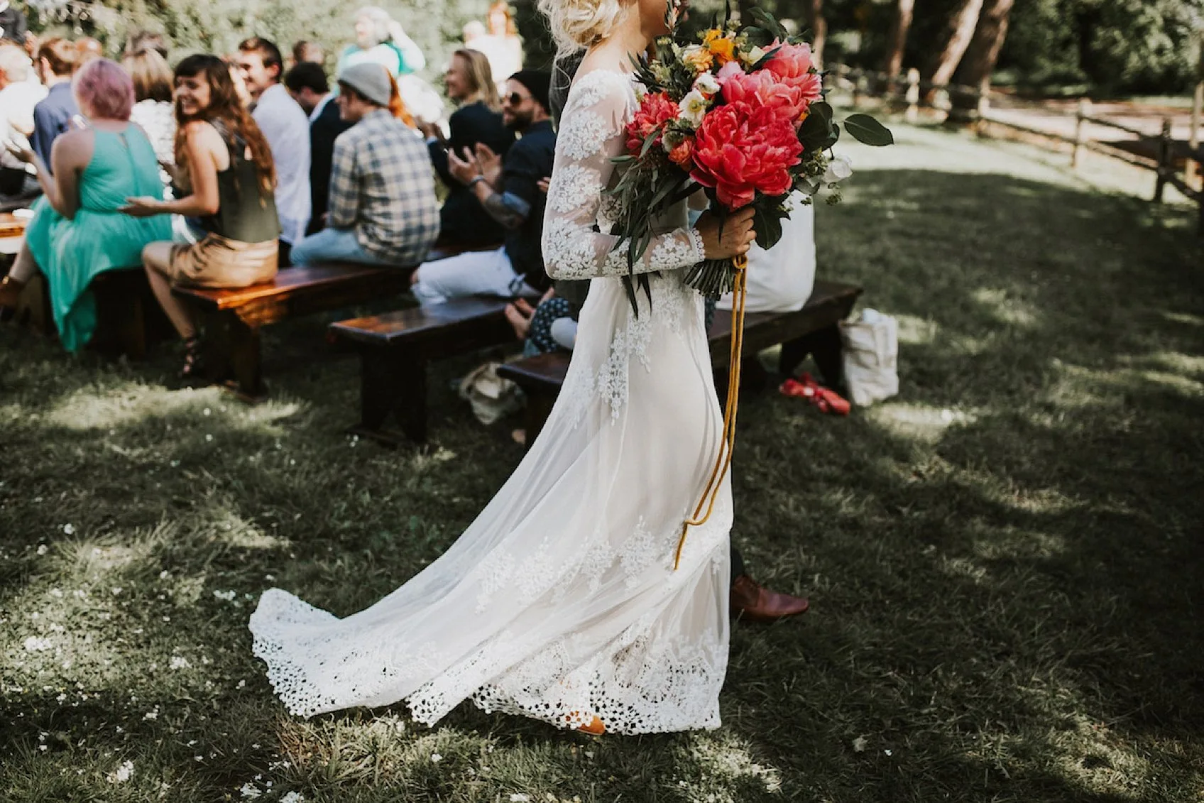 A bride carrying a bright bouquet past applauding guests