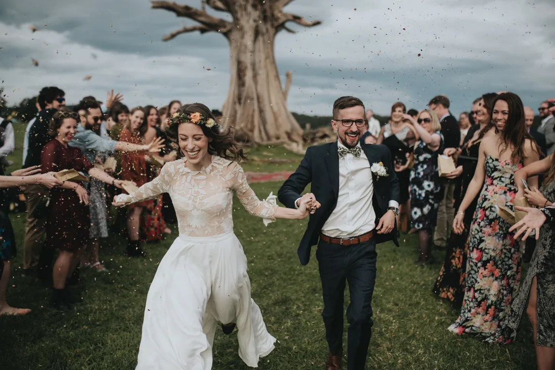 Couple walking back down the aisle through confetti beneath an old fig