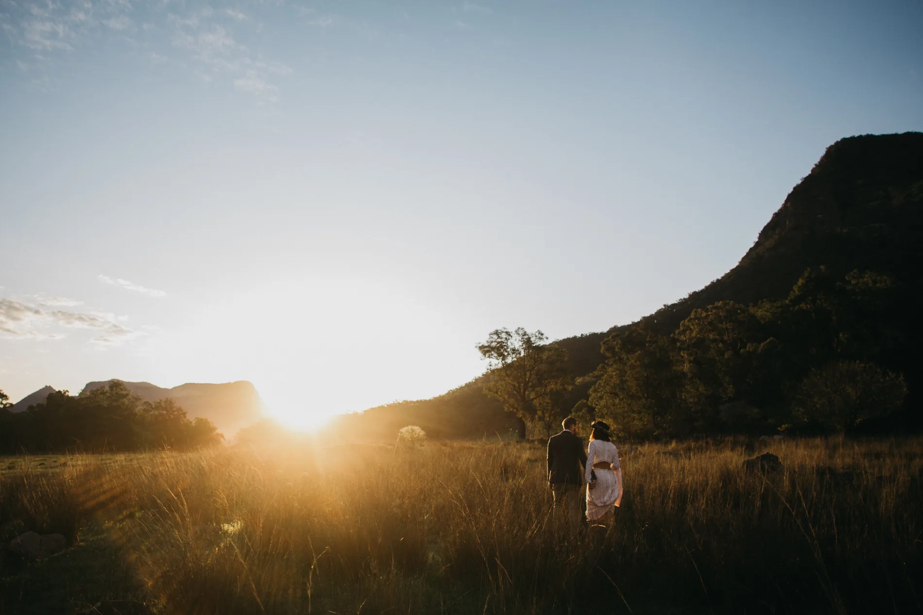 Two figures walking toward the sun in a wide valley