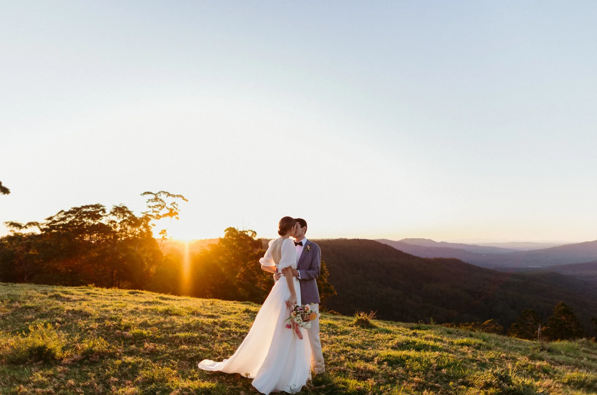 Two people on a ridge line as the sun drops behind the range